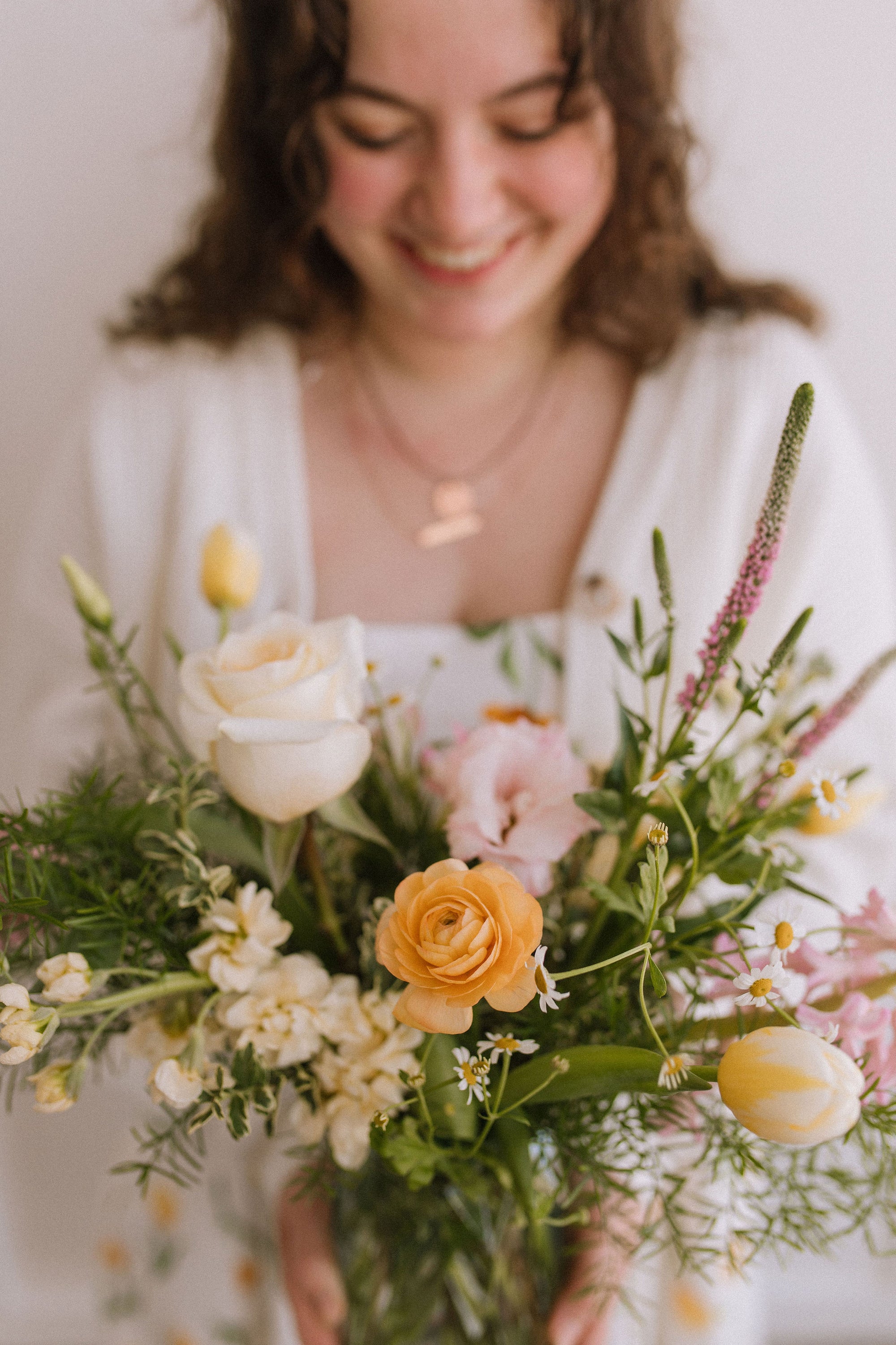 Woman smiling holding a bouquet of spring flowers in a vase 