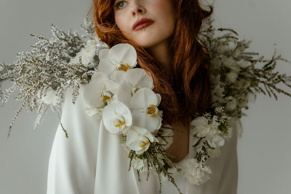 Woman with red hair and a blazer with a floral collar of orchids, calcynia, white carnations, and white delphinium 